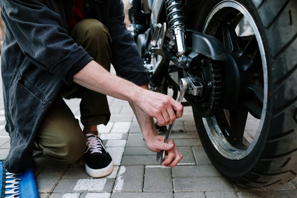 Close-up of a mechanic adjusting a motorcycle wheel with a wrench, outdoors.