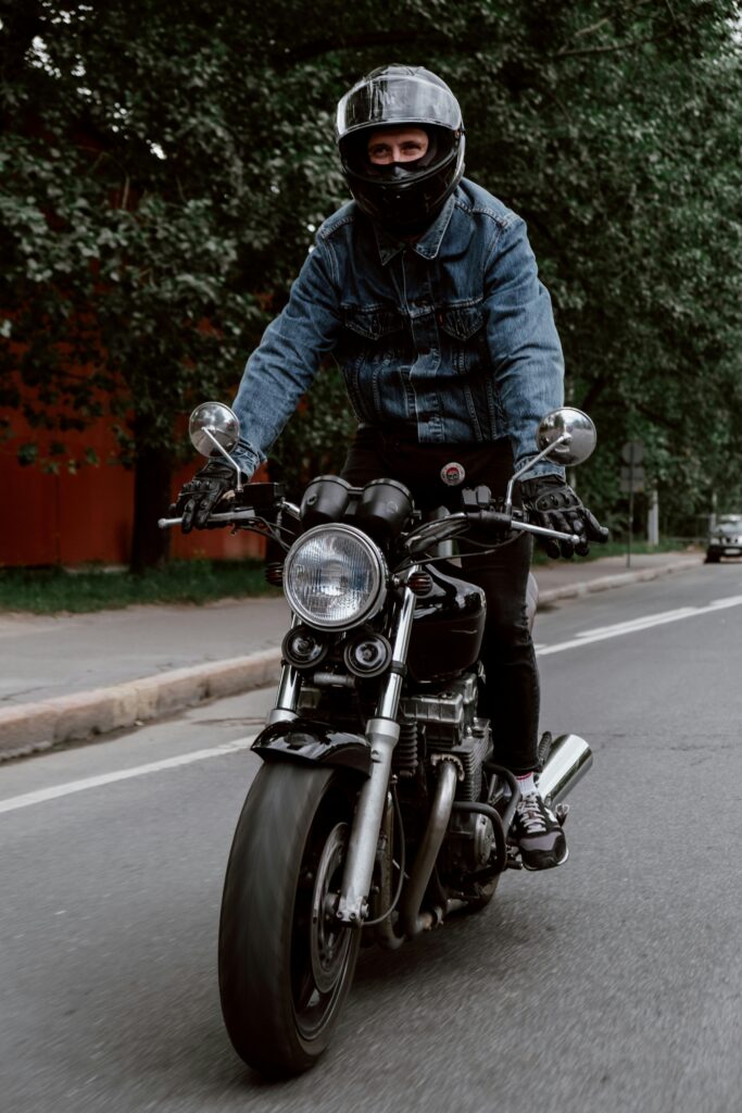 Adult male motorcyclist riding a classic motorcycle on a city street wearing a protective helmet.